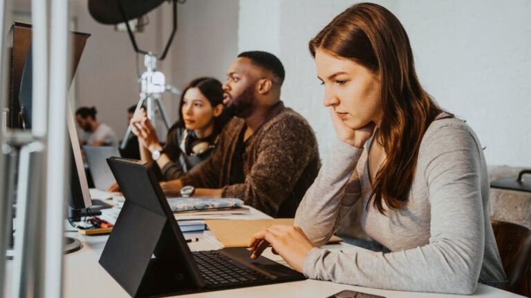 A male and two female in an office sitting in front of computers